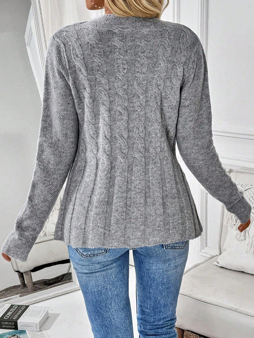 Back view of a grey cable knit cardigan with a ribbed hem