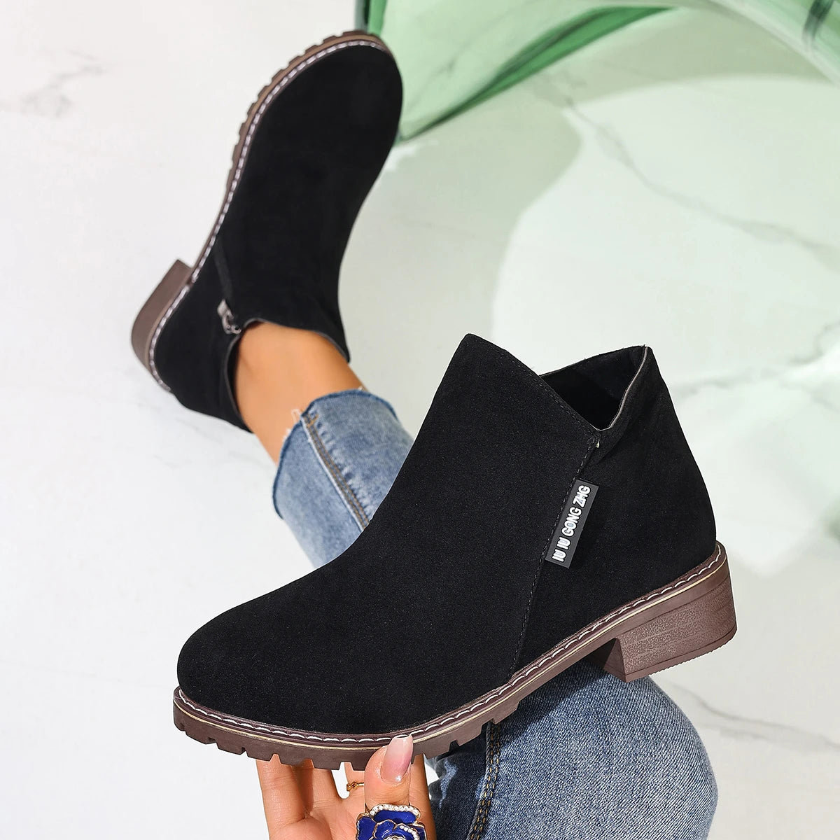 Black ankle boots held in hand, close-up