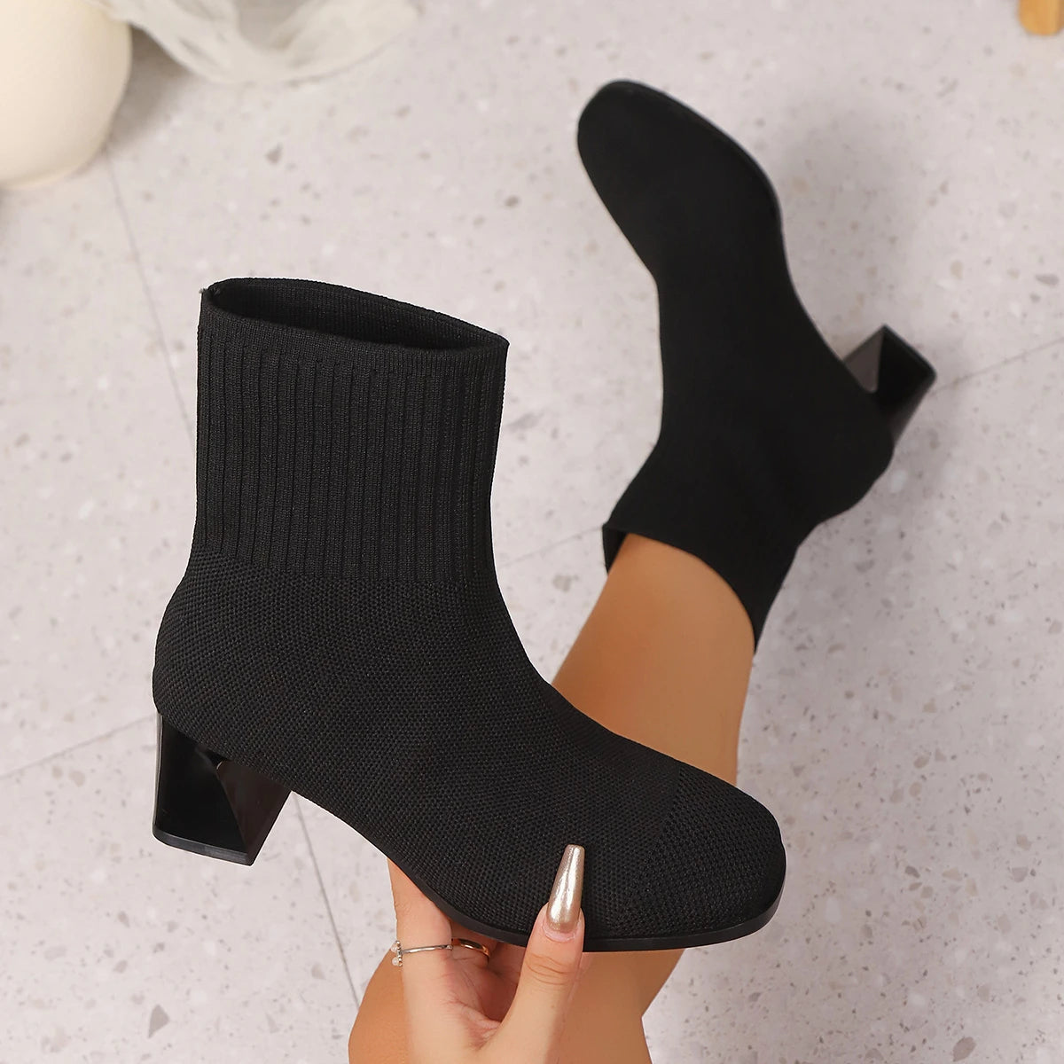 Black knit sock ankle boots with block heel, held in hand, close-up