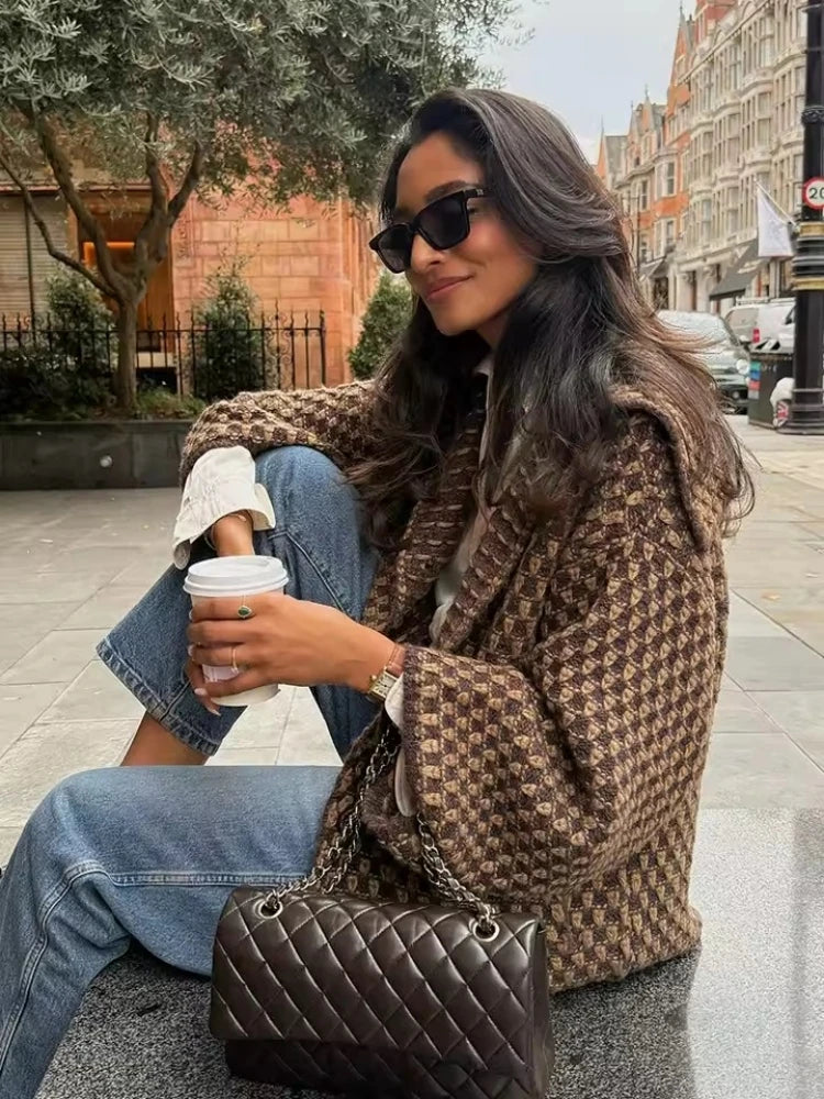 Brown check knit cardigan worn seated with jeans