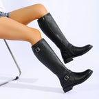 Black knee high boots with buckle straps and low heel, worn seated