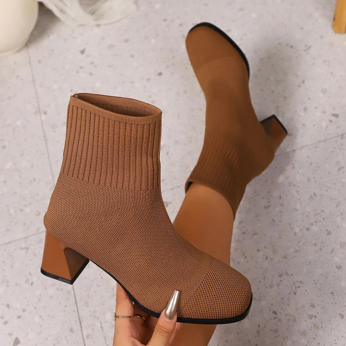 Tan brown knit sock ankle boots with block heel, held in hand, close-up