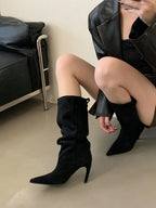 Black flock slouch knee high boots with pointed toe and thin heel, worn