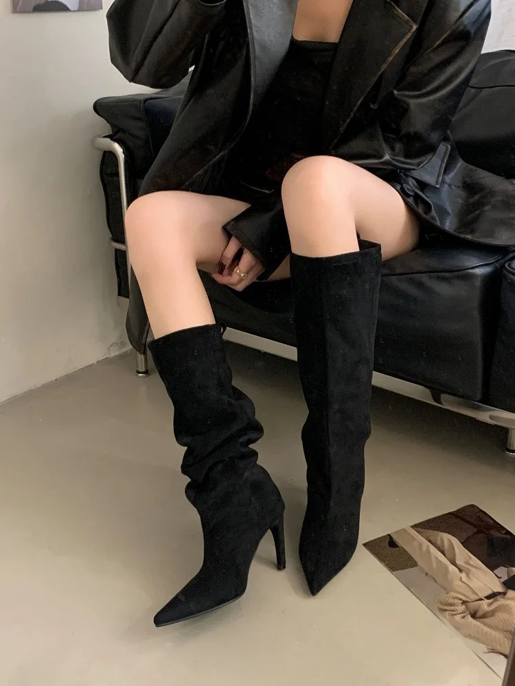 Black flock slouch knee high boots with pointed toe and thin heel, worn