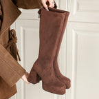 Brown platform knee high boots with chunky block heel, held in hand