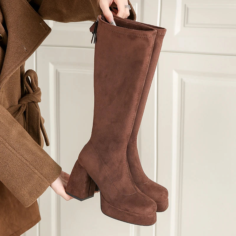 Brown platform knee high boots with chunky block heel, held in hand