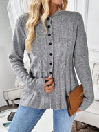 Grey cable knit cardigan with black buttons worn open at the hem
