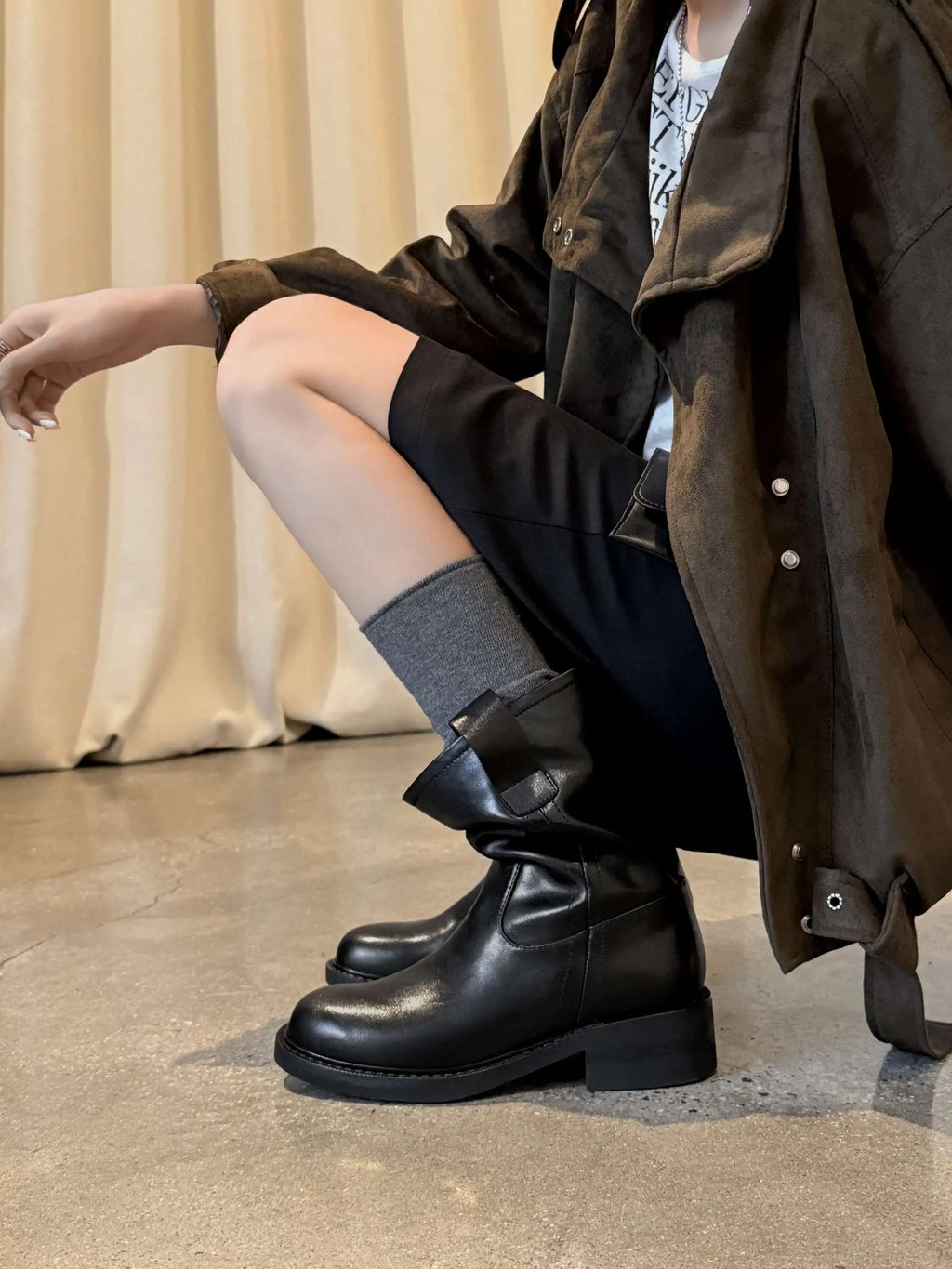 Black leather mid calf western boots worn crouching with an oversized jacket